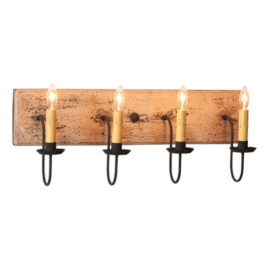 A four-light vanity light fixture with a heavily distressed painted finish in a buttermilk color, featuring textured arms with crimped pans and hanging from a wood panel.