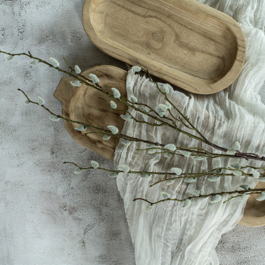 A cream pussy willow branch with delicate flowers arranged on a wooden surface with a textured white fabric.