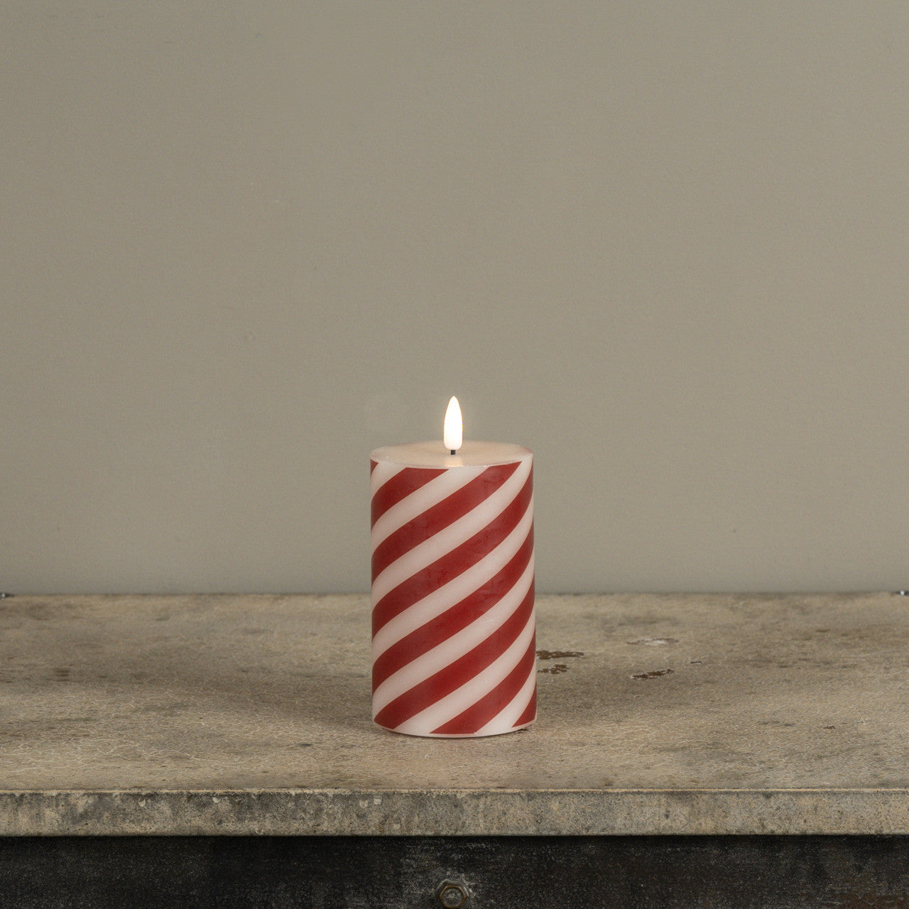 Red and white striped candle on a wooden surface with a gray background