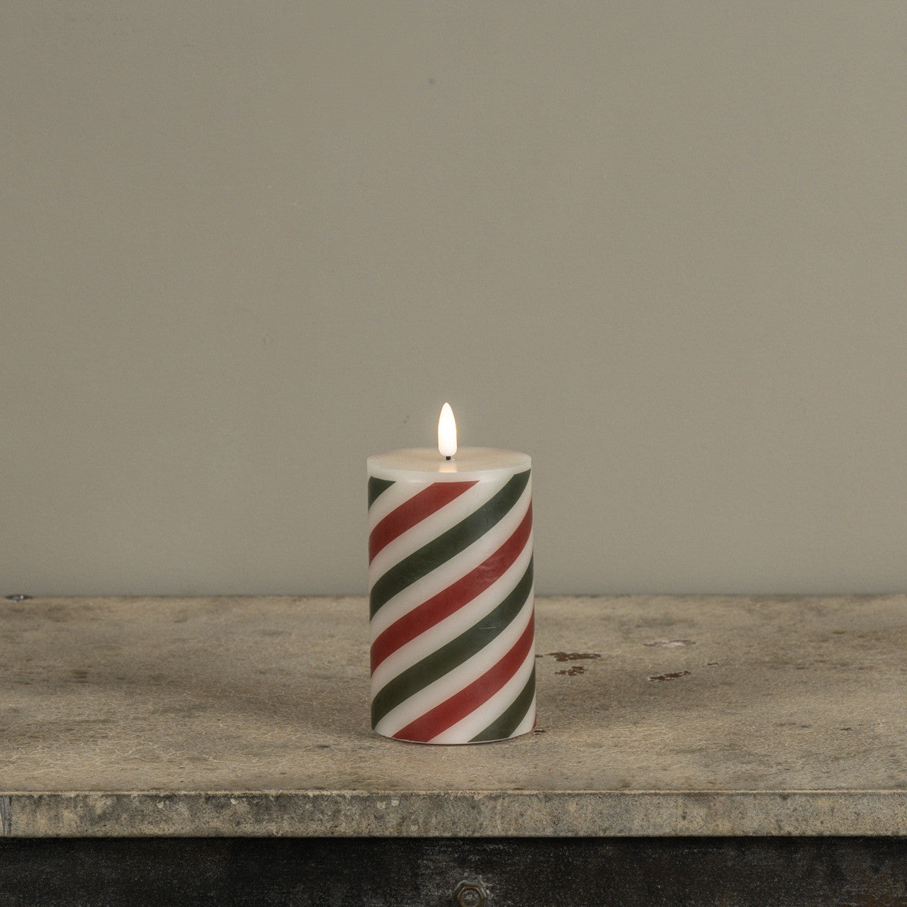 Striped candle with red and green patterns on a wooden surface against a gray background