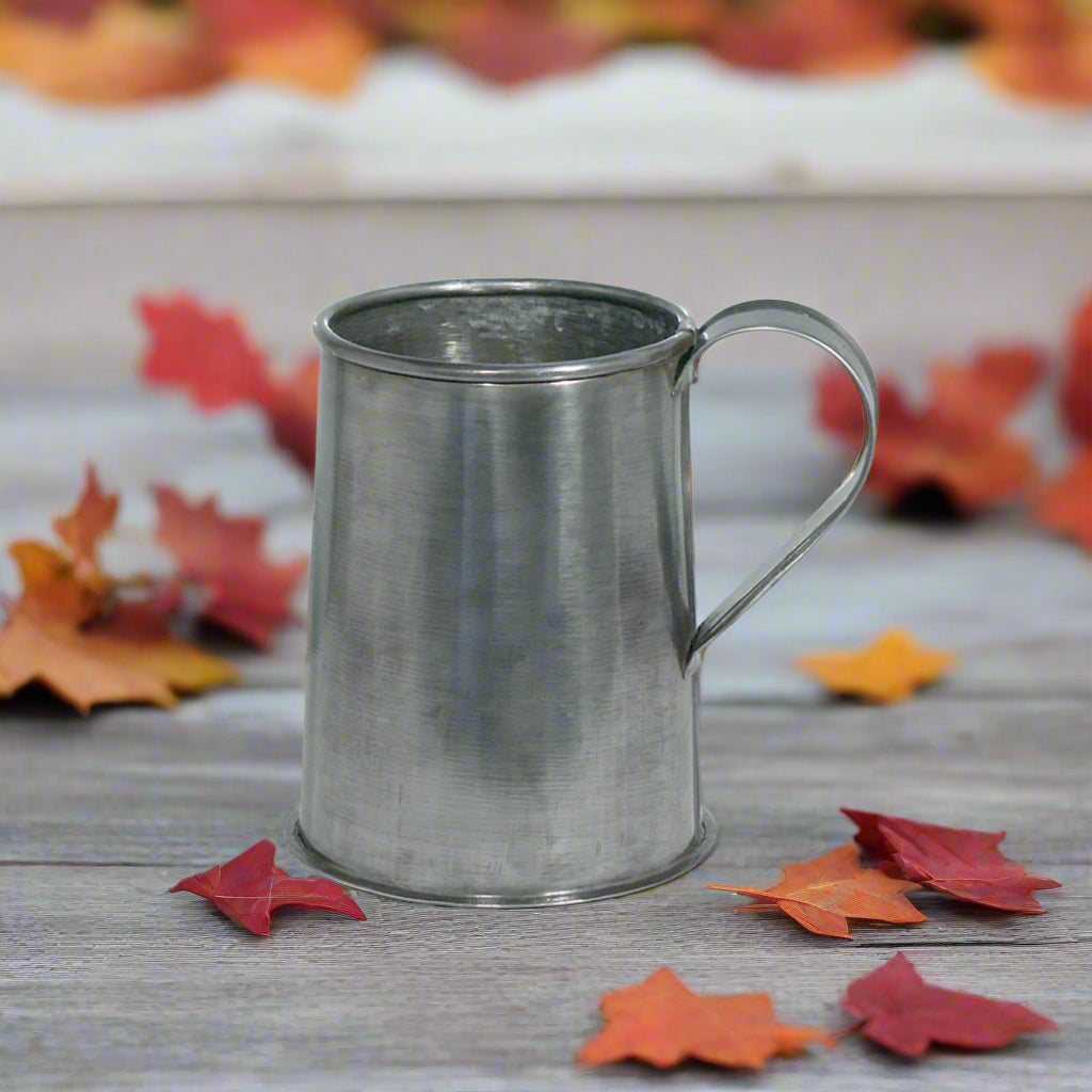 A 5-inch tall tin pint tankard made of tin with a handle on the side in a fall setting.
