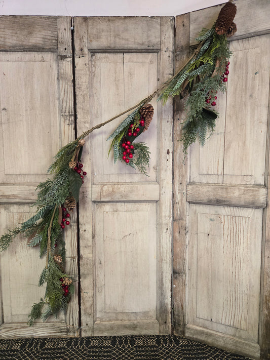 Decorative Christmas garland with pine cones and red berries on a rustic wooden door.