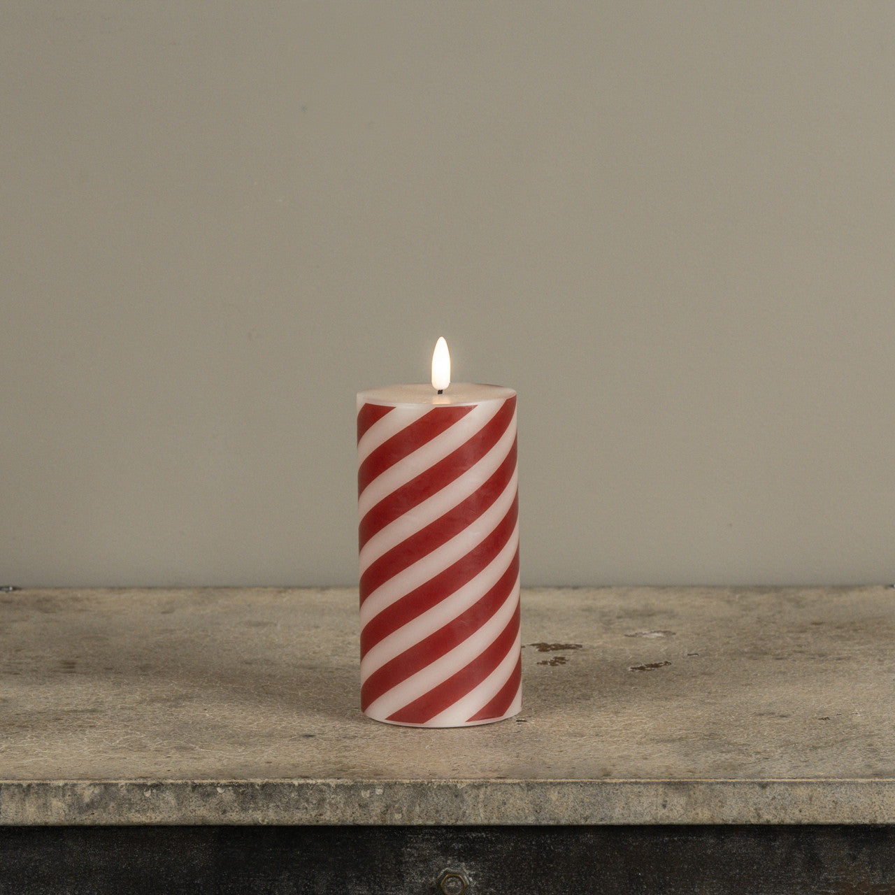 Red and white striped candle on a wooden surface with a neutral background