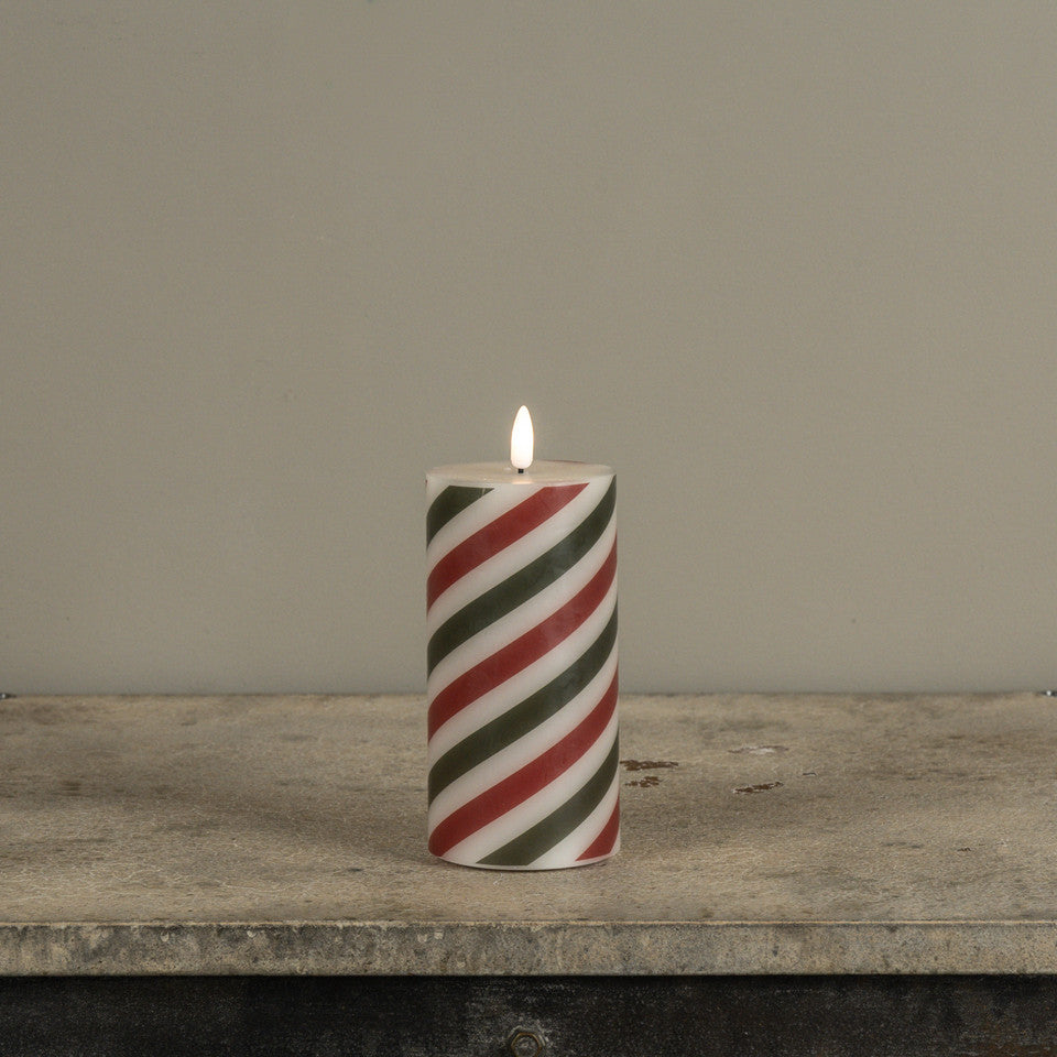 Striped candle with red and green pattern on a wooden surface