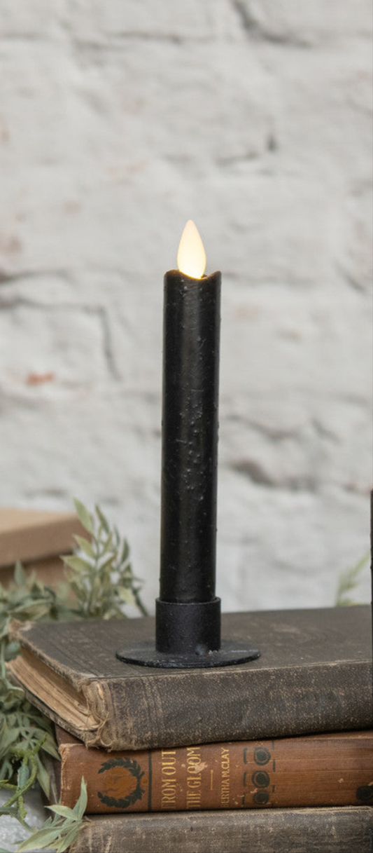 A black taper candle with a moving flame design, placed on a surface with a rustic appearance.