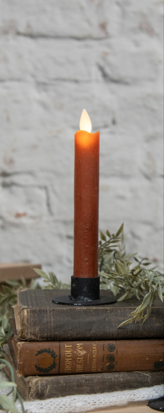 A 6.75 inch moving flame bronze taper candle lit and placed on a stack of old books with a brick wall in the background.