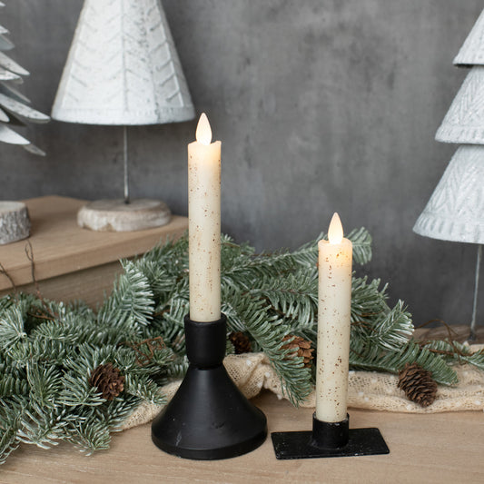 Two candle lights on stands with Christmas decorations in the background