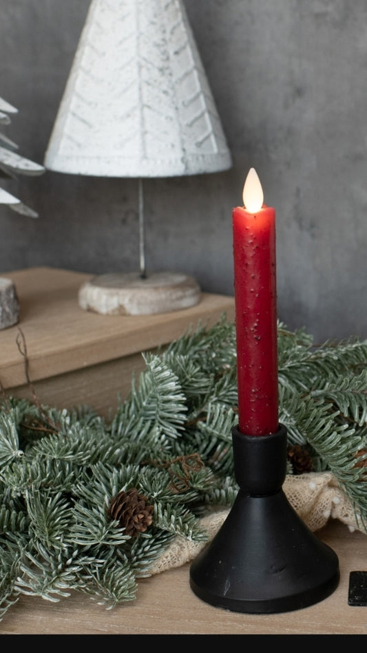 Red candle on a black holder with a white textured lamp in the background