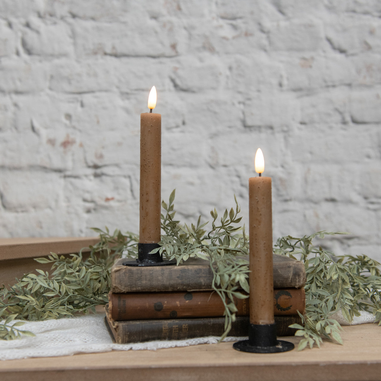 Two lit candles on vintage books with greenery against a stone wall background