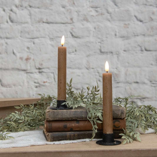 Two lit candles on vintage books with greenery against a stone wall background