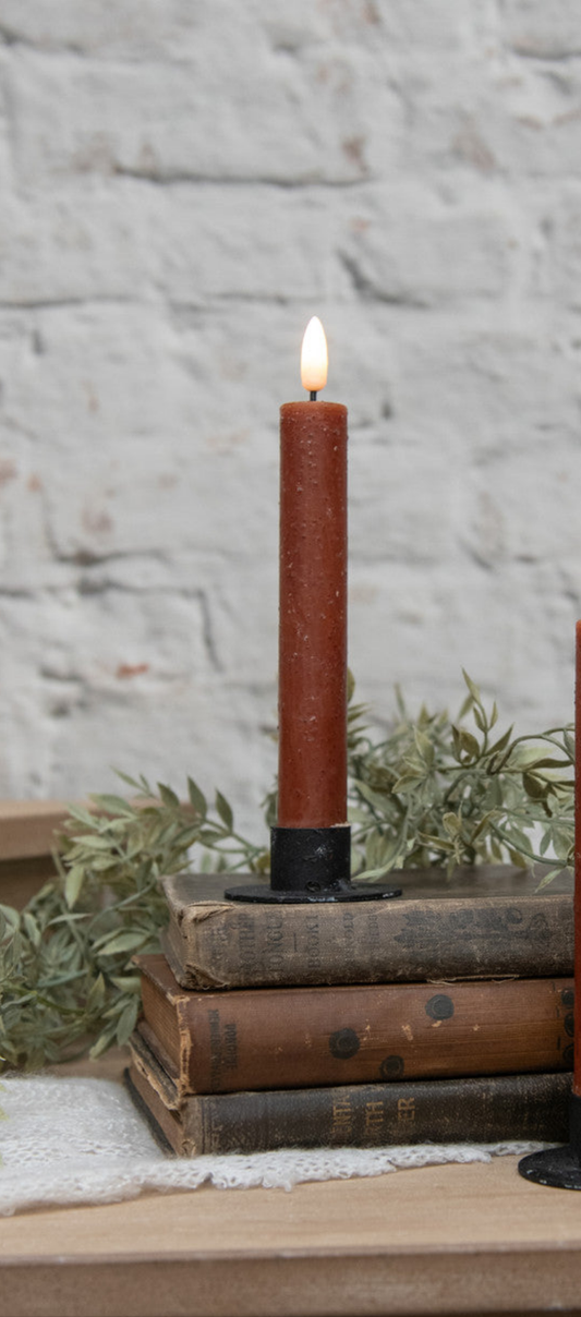 A 7-inch bronze taper candle with a 3D flame design, sitting on a stack of books, with a lit flame on top.
