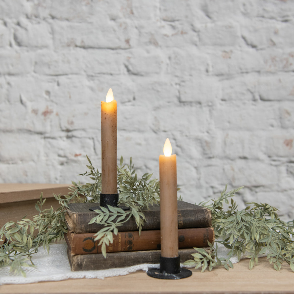 Two lit candles on vintage books with greenery against a stone wall background