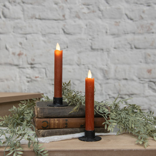 Two lit candles on stacked books with a stone wall background