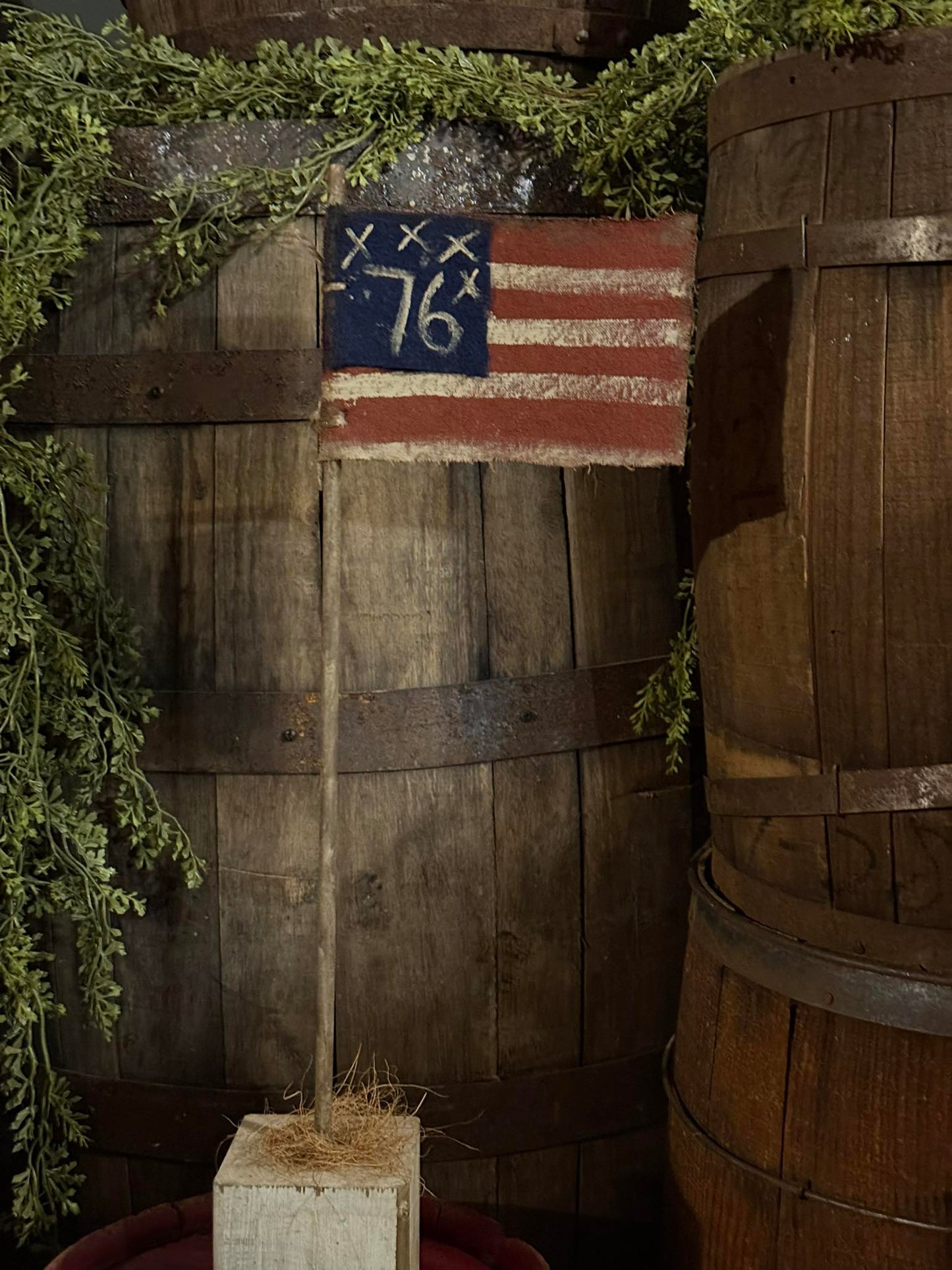 Vintage-style American flag with '76' on a wooden post against a rustic wooden wall.