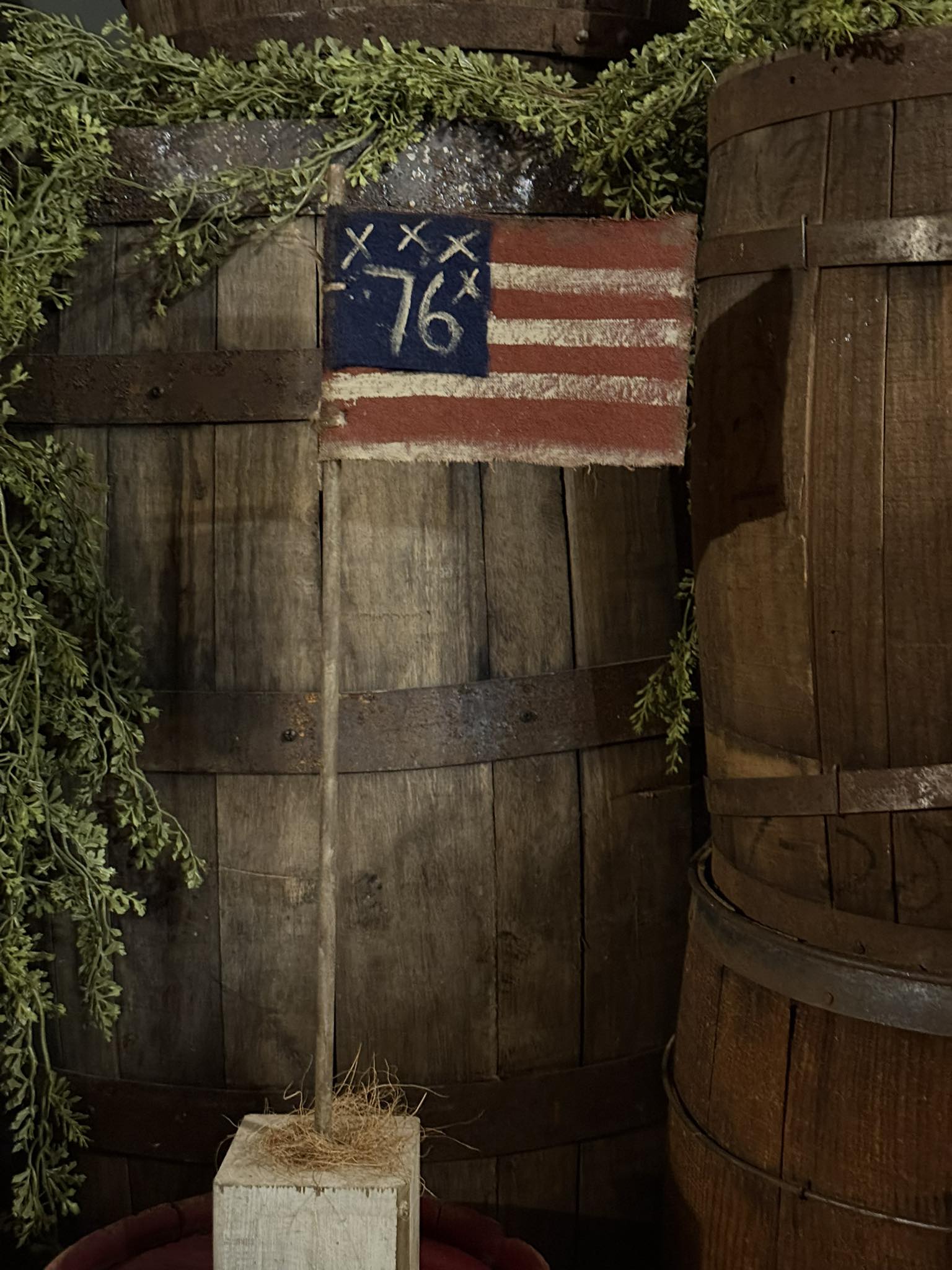 Vintage-style American flag with '76' on a wooden post against a rustic wooden wall.