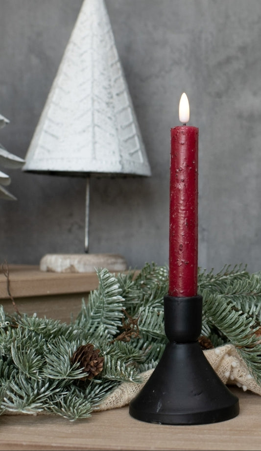 Red candle in a black holder with a Christmas tree and decorations in the background