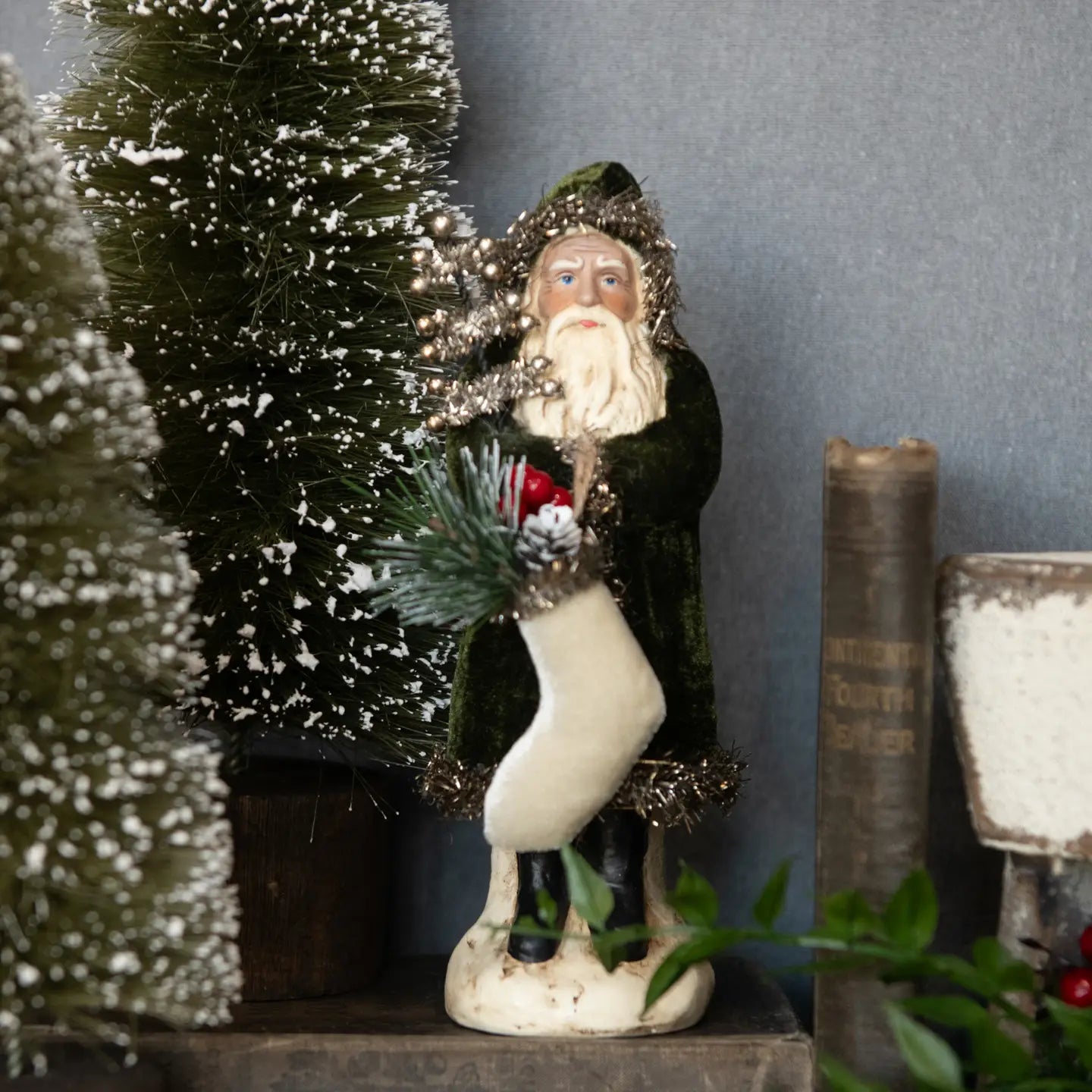 Decorative figure of a winter scene with a person in a coat and hat, surrounded by small trees and books.