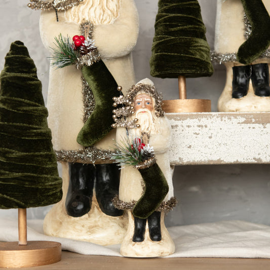 A collection of holiday ornaments featuring a belsnickel figure in oatmeal velvet material, with decorative Christmas trees in the background.