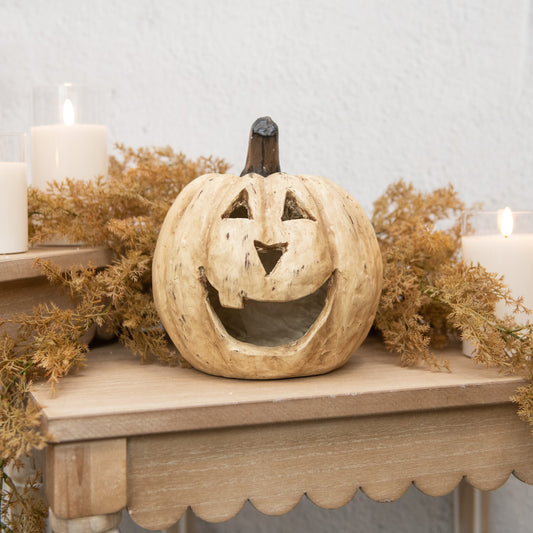 Wooden pumpkin decoration on a mantelpiece with candles and dried foliage.