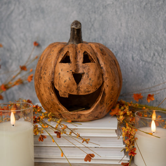 Decorative pumpkin with a carved face on books with candles and autumn leaves.