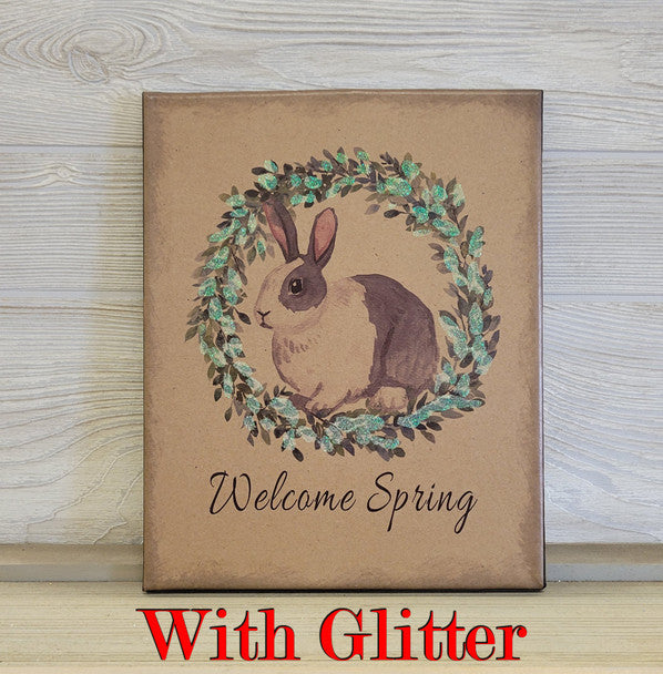 Decorative sign with a rabbit illustration and 'Welcome Spring With Glitter' text on a wooden surface.