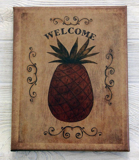 A canvas print featuring a pineapple motif with the word 'Welcome' written above it, set against a wooden background.