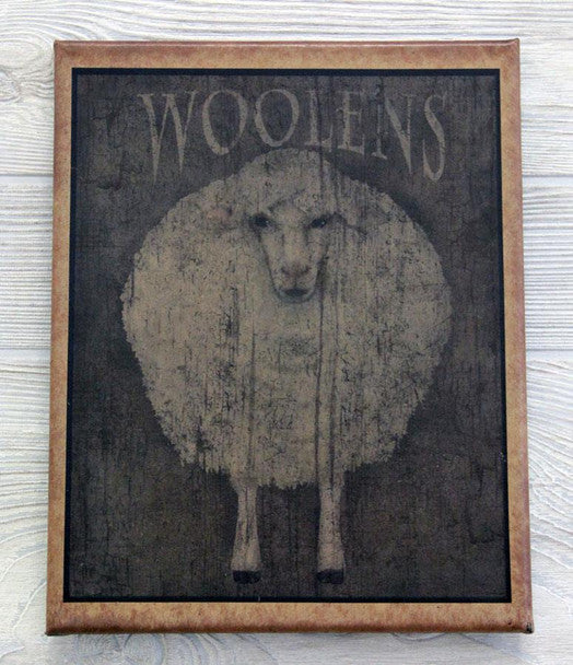 A canvas print featuring the word 'Woolens' with an image of a sheep in the center, framed in a simple brown wood frame.