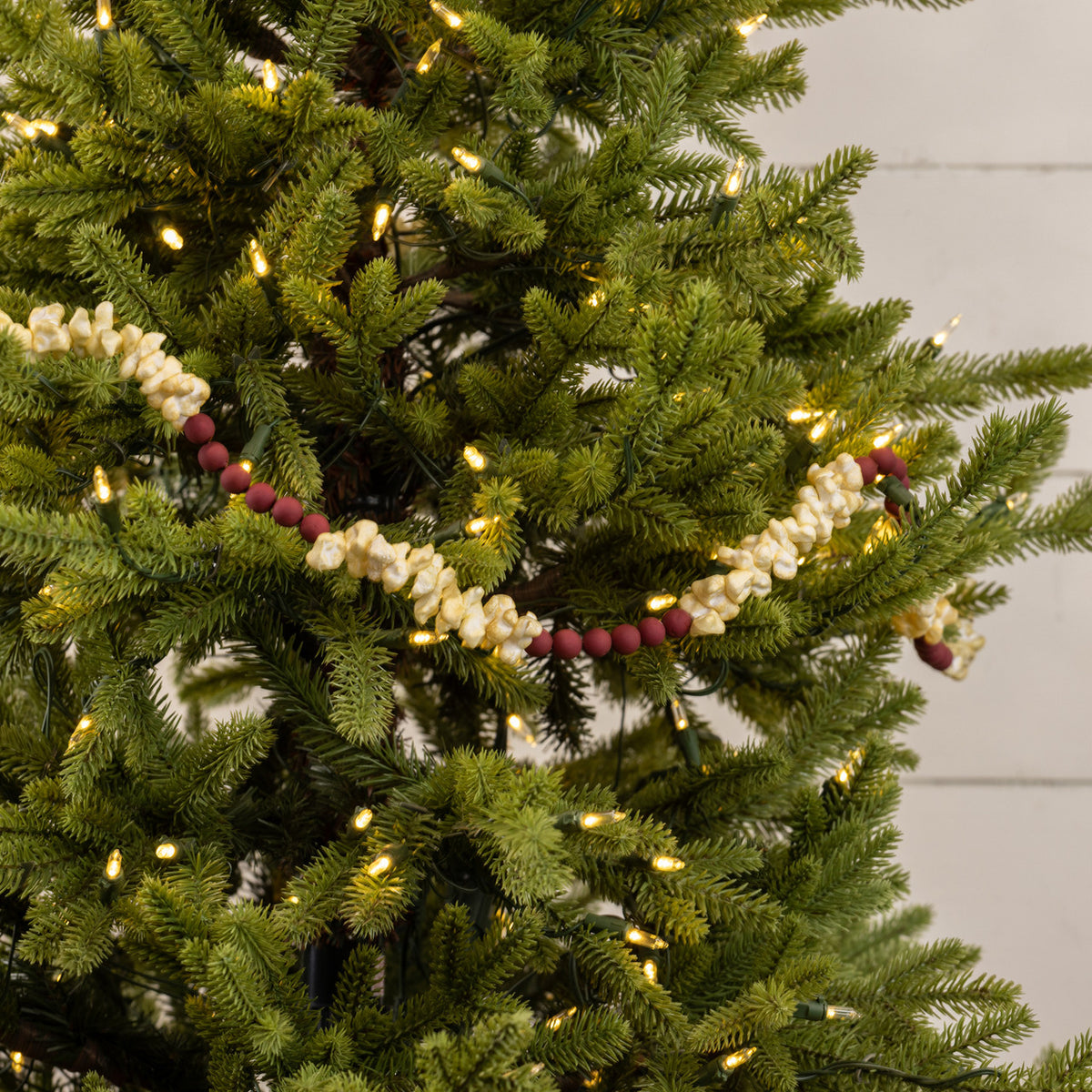 Decorative pearl and berry garland on a Christmas tree with lights.