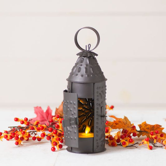 Paul revere lantern with candle inside and orange flowers in background.
