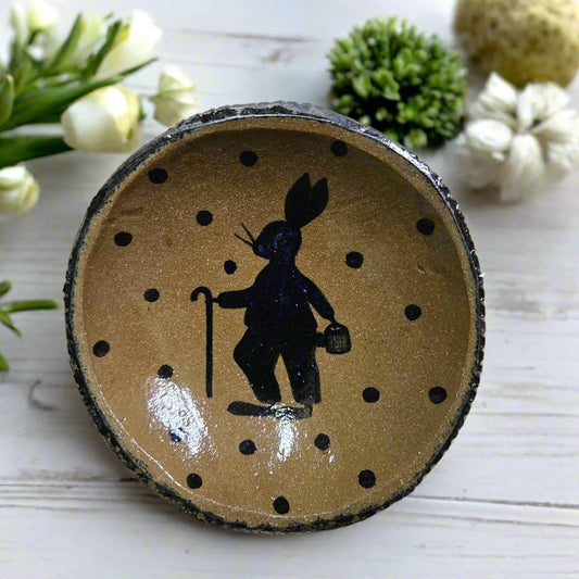 A round stoneware plate with the silhouette of a rabbit and cane on it, featuring a polka dot motif. Brown in color with a black rim.
