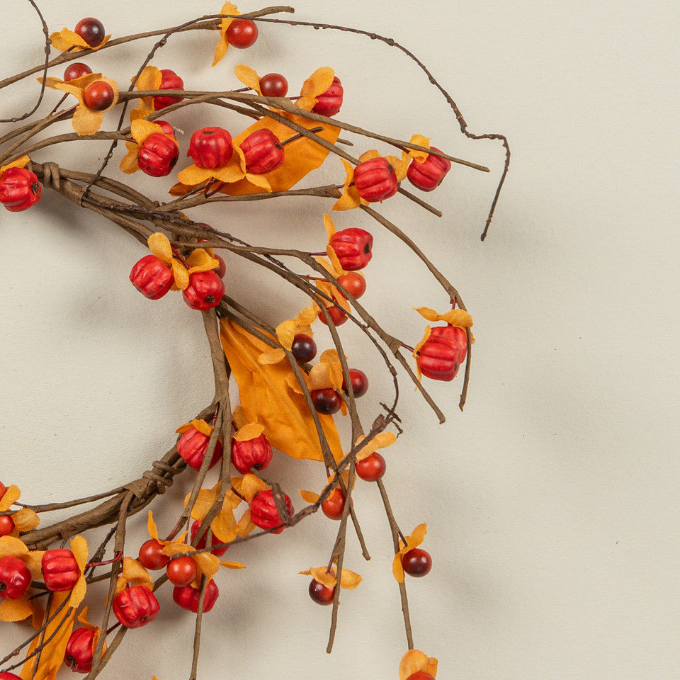 Decorative wreath with red berries and orange leaves on a beige background