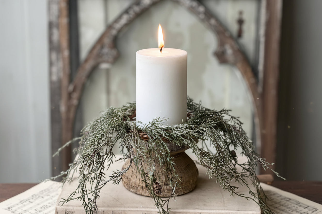 White candle on a wooden block with greenery, placed on vintage books against a rustic background.