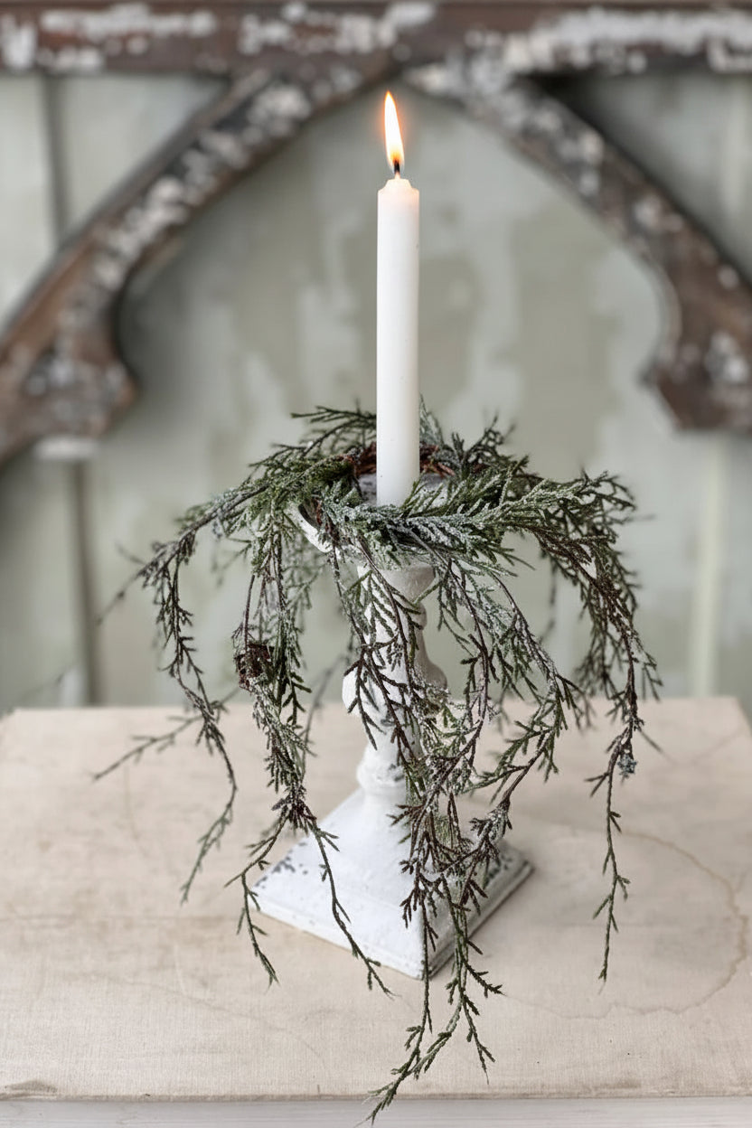 Decorative candle holder with greenery and a white candle on a textured surface.