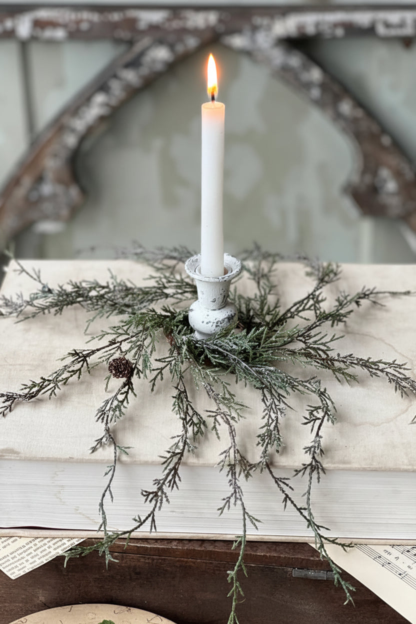 White candle in a rustic holder with greenery on an old book against a decorative mirror background