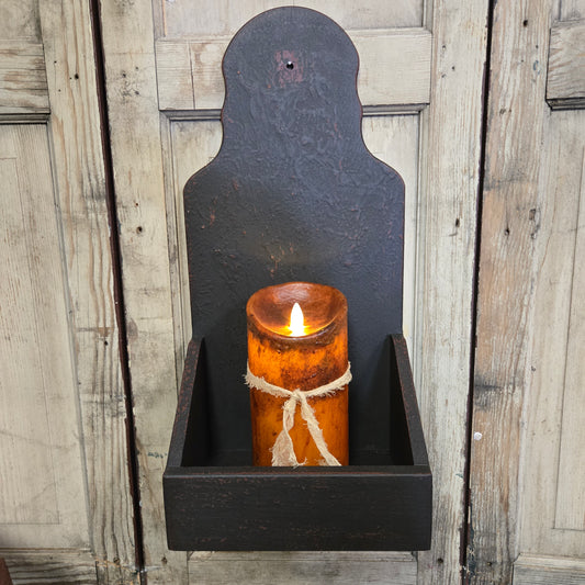 A black wooden sconce candle holder mounted on a wall, holding a candle with a warm glow.