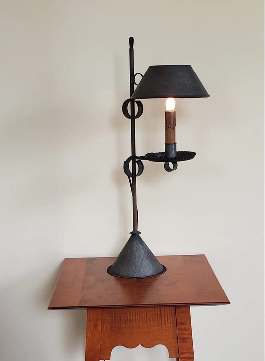 A black tin table light with a geometric design, featuring a lamp on top supported by a metal stand, placed on a wooden table.
