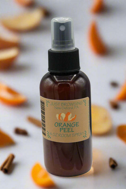 Bottle of orange peel room spray with a label on a surface with orange peels and cinnamon sticks.
