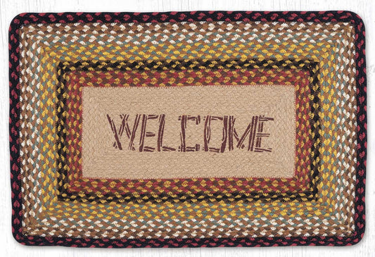 A rectangular braided jute doormat with a rustic folk design. The center features a natural beige woven background with the word 'WELCOME' spelled out in dark brown.