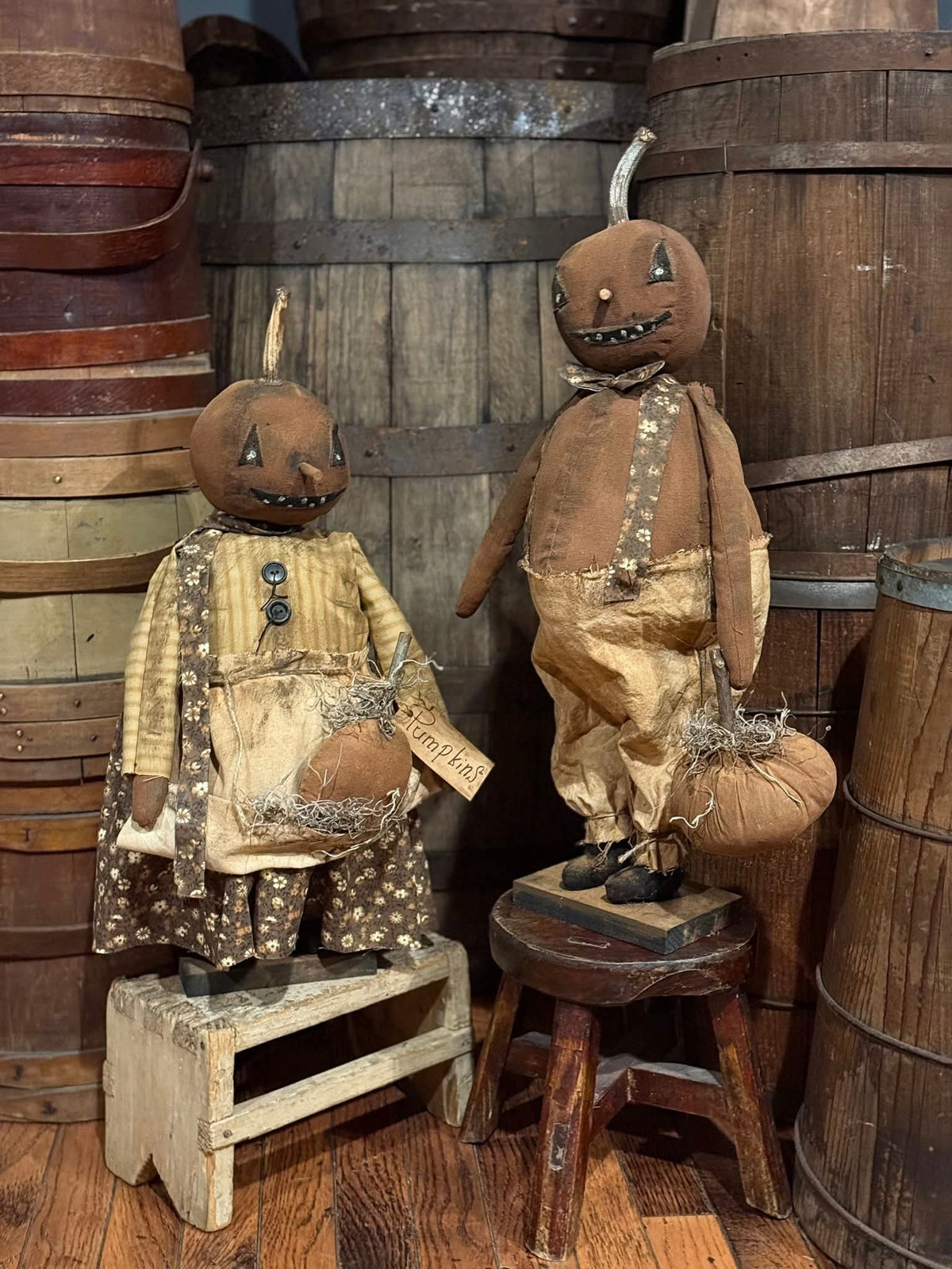 Two vintage-style scarecrow figures in a rustic setting with wooden barrels.