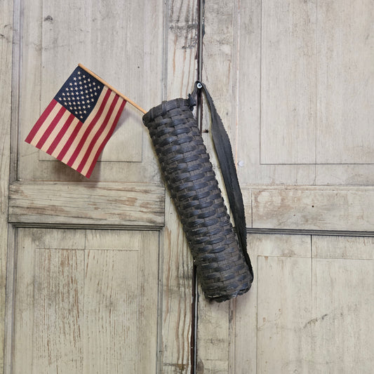 A brown woven basket with a handle, displayed against a wooden background, with a small American flag positioned to its side.