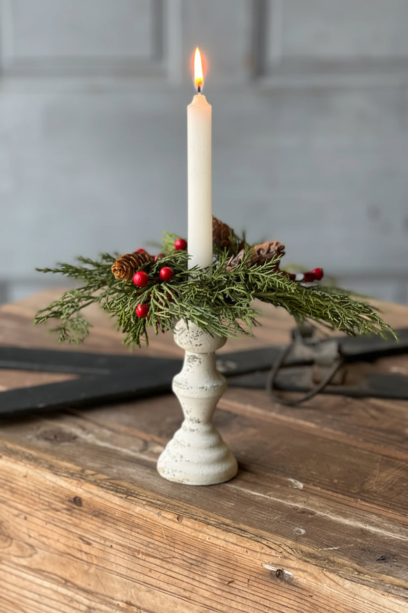 Decorative candle holder with a candle, greenery, and berries on a wooden surface.