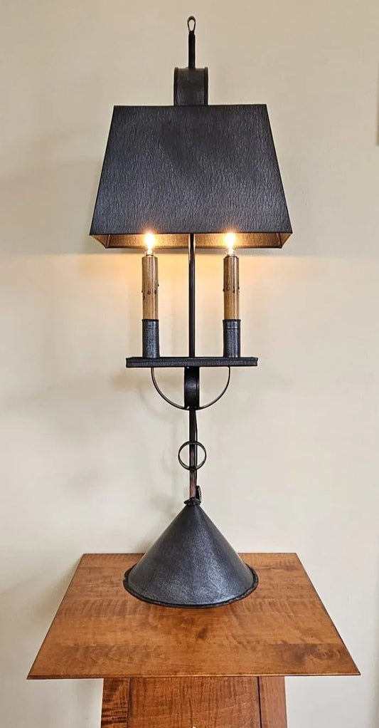 Decorative lamp with a black shade and metal base on a wooden table against a beige wall.
