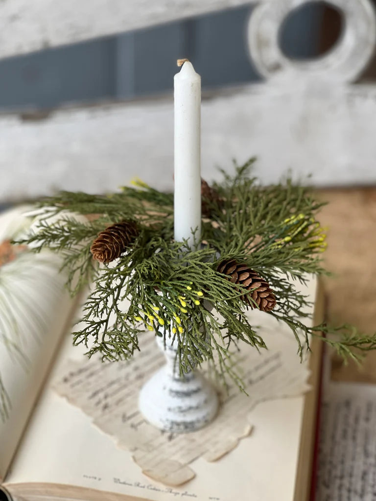 A candle ring with cedar greenery and pine cones, placed on an open book.