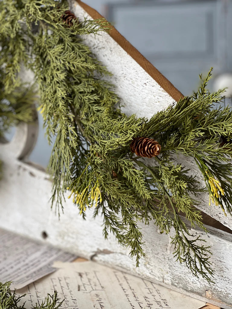 Green pine garland with pinecones on a wooden mantel.