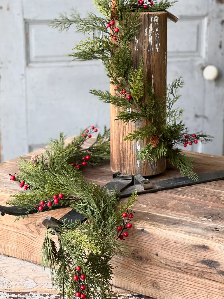 Decorative arrangement of greenery with red berries on a wooden surface.