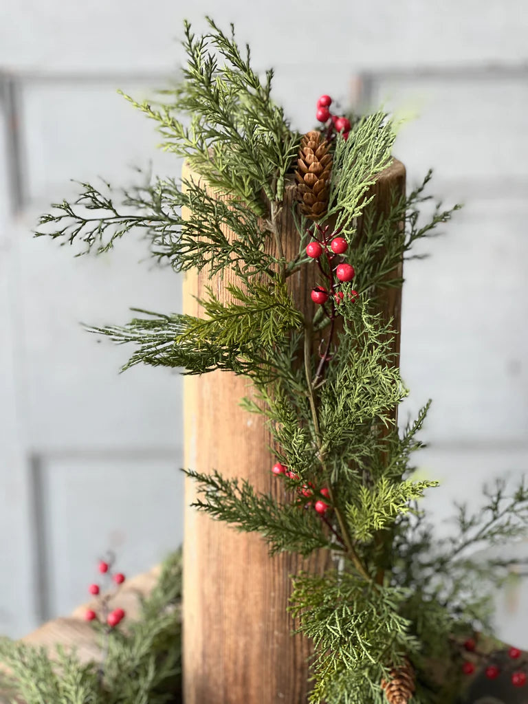 Decorative arrangement of greenery and red berries on a wooden post with a light gray background.