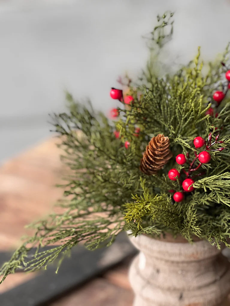 Bouquet of greenery with red berries and a pine cone in a rustic vase.