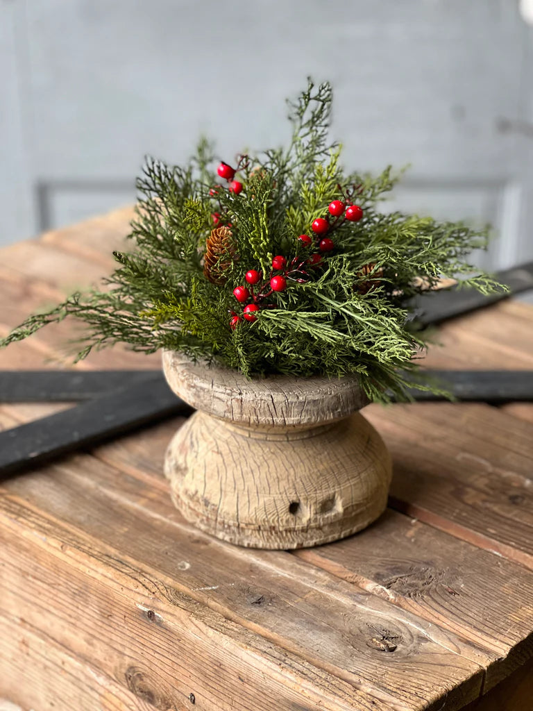 A decorative half sphere floral arrangement featuring green foliage and red berries, placed on a rustic wooden table.