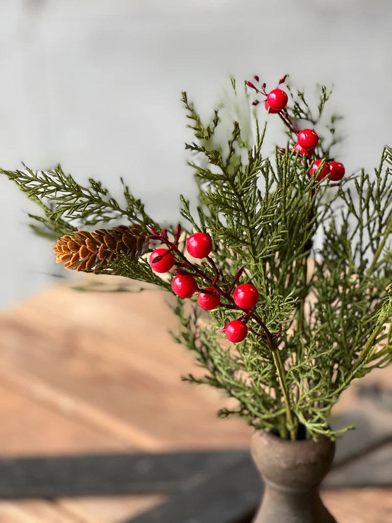 Decorative arrangement with greenery and red berries in a vase on a wooden surface.