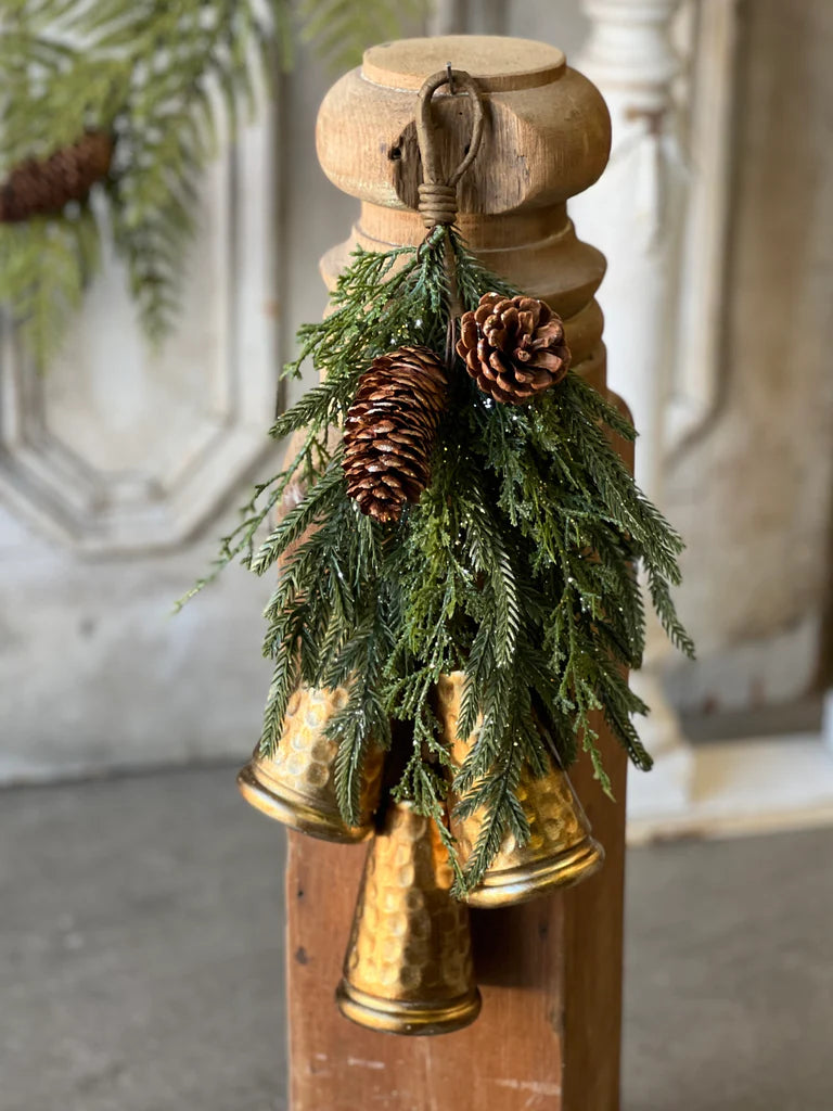 Decorative wooden post with gold bells and pine cones against a neutral background